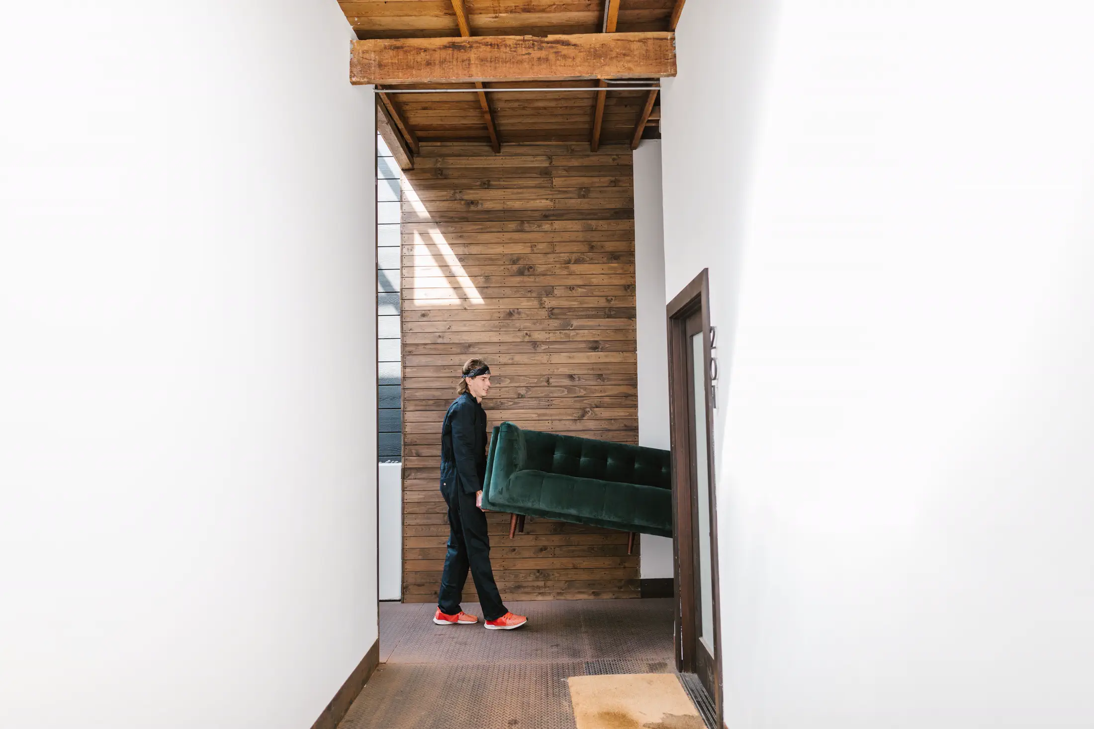 Mover carrying a green sofa through a narrow interior route